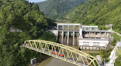 本名ダムを背景に第６只見川橋梁（きょうりょう）を走る只見線の列車。自然と人工物が共存している。ダムの上を旧国道２５２号が通る、全国でも珍しい造りだ＝金山町本名（ドローン撮影）