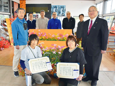 感謝状を受けた佐川さん（前列左）、伊成さん（同右）。中心の造花は２人の飾り付けによるもの